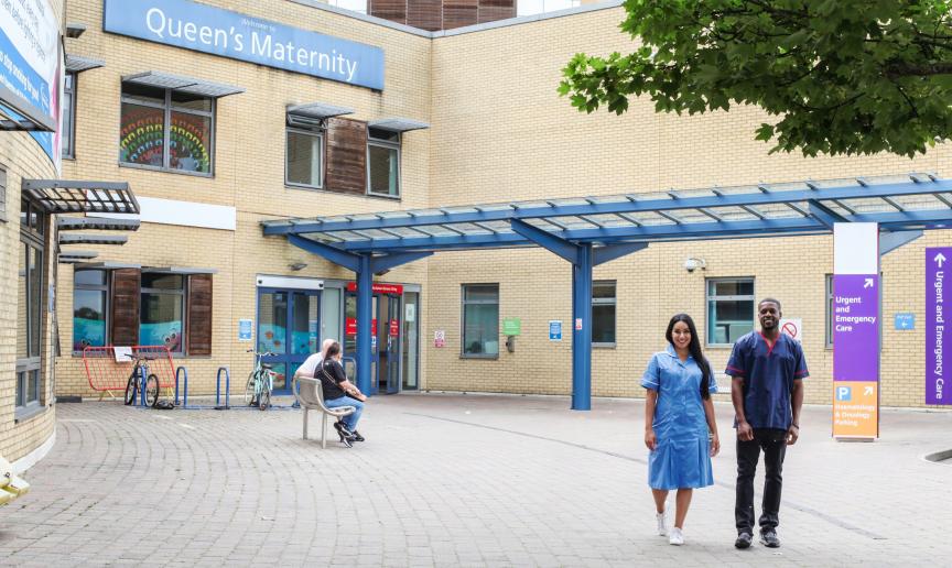 A male and female colleague stood outside a hospital smiling together